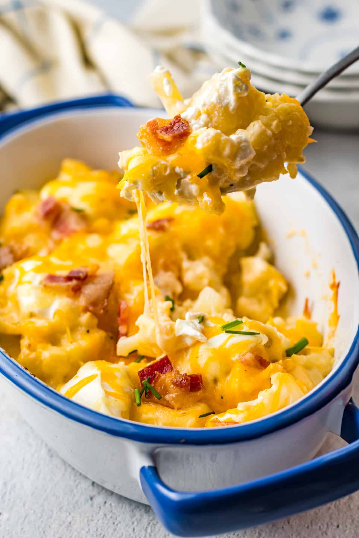 a spoonful of loaded cauliflower bake hovering over loaded cauliflower bake in a blue and white casserole dish.