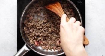ground beef in a skillet with a hand holding a wooden spoon