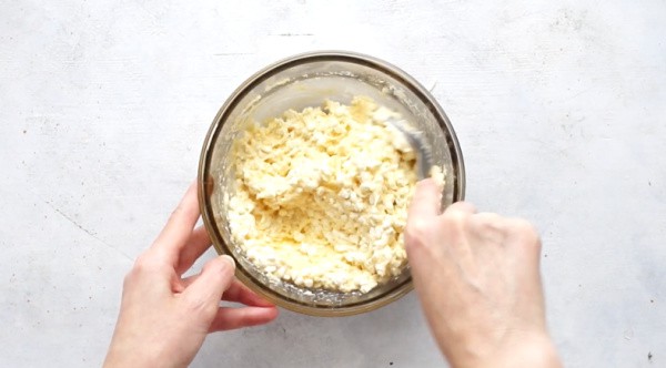 hands mixing cheese filling in a glass bowl for stuffed shells