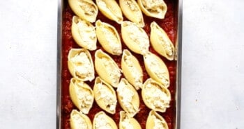 pasta shells stuffed with cheese filling on top of marinara sauce in a baking dish