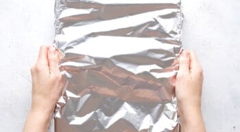 hands covering baking dish with aluminum foil