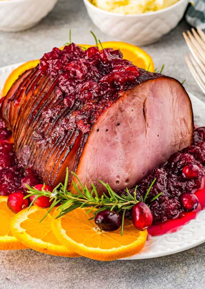 cranberry glazed ham on a white serving platter with orange slices