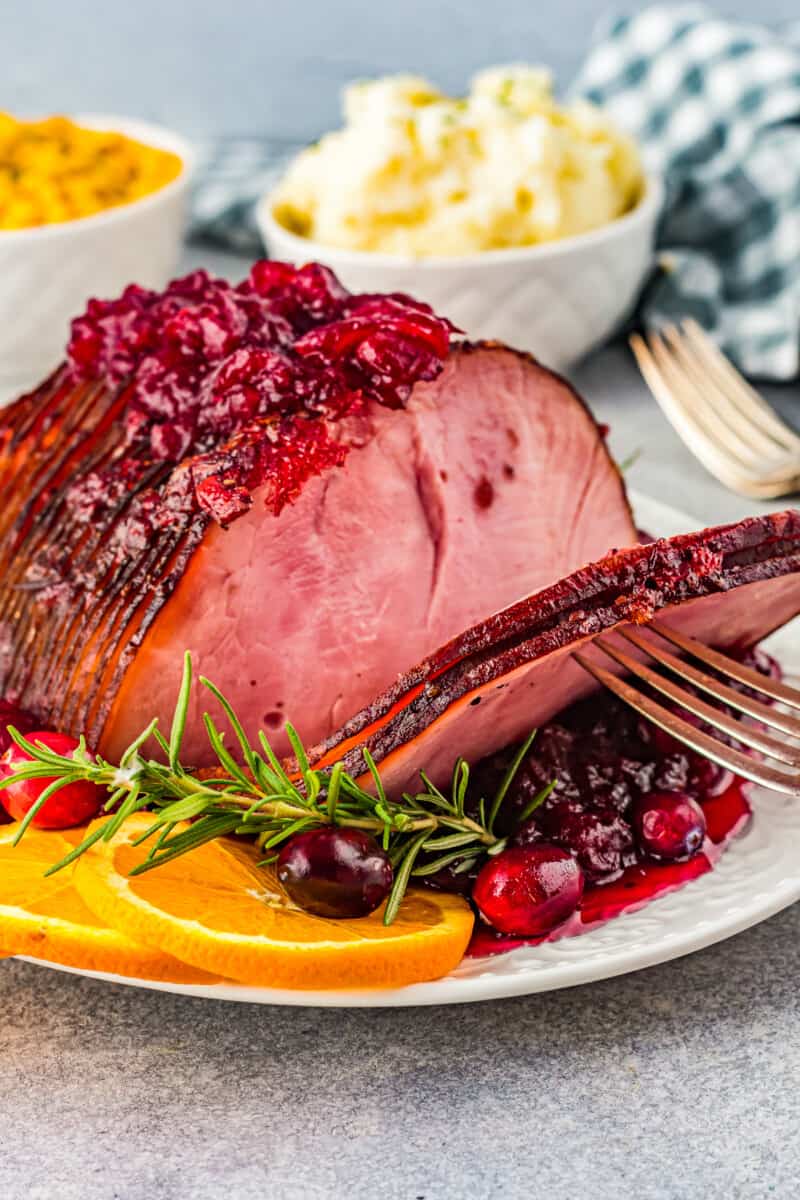 fork grabbing slices of cranberry glazed ham on a white serving platter