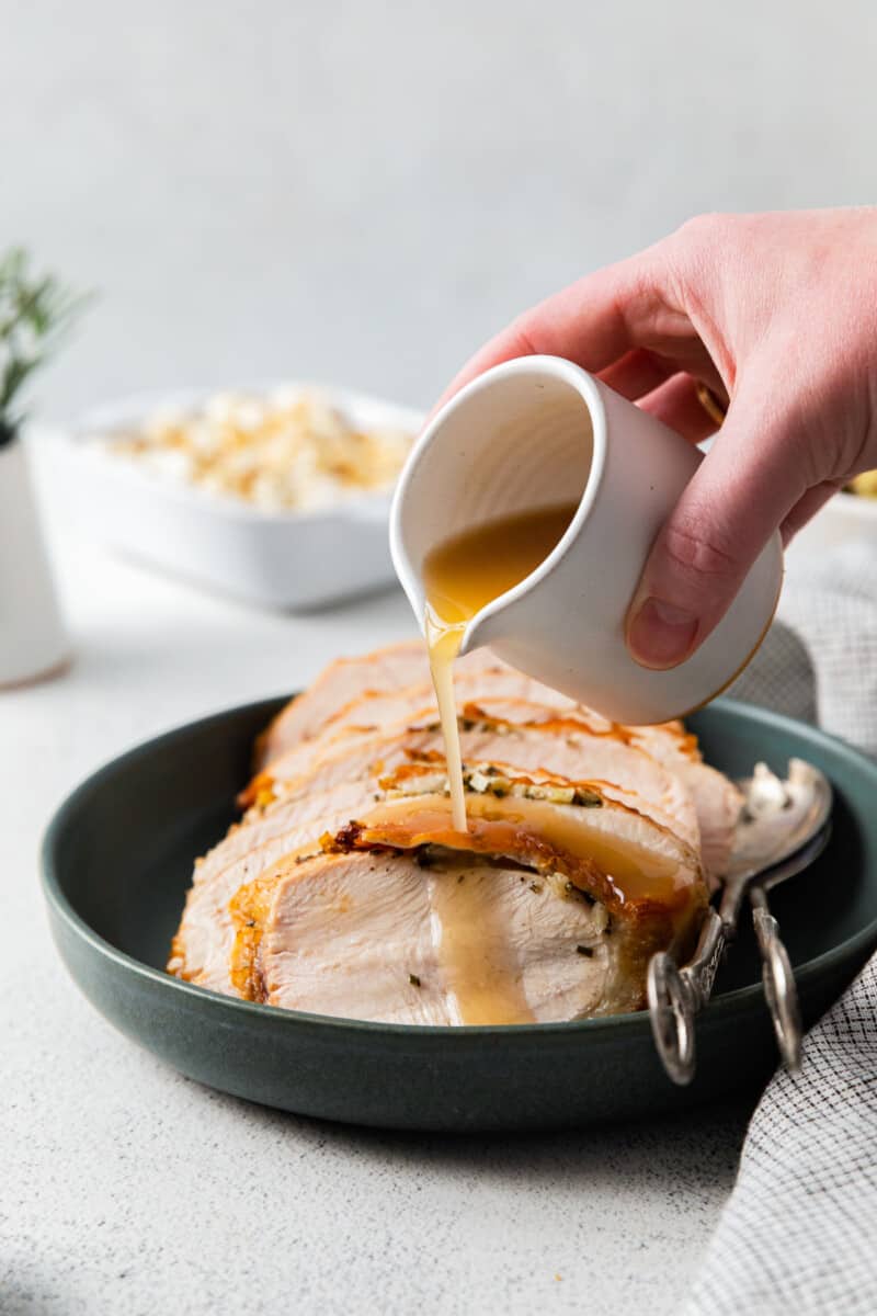 hand pouring gravy onto sliced turkey breast on a plate