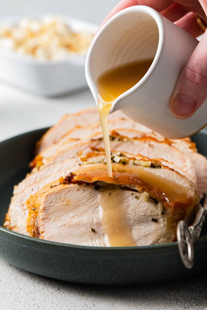 hand pouring gravy onto sliced turkey breast on a plate