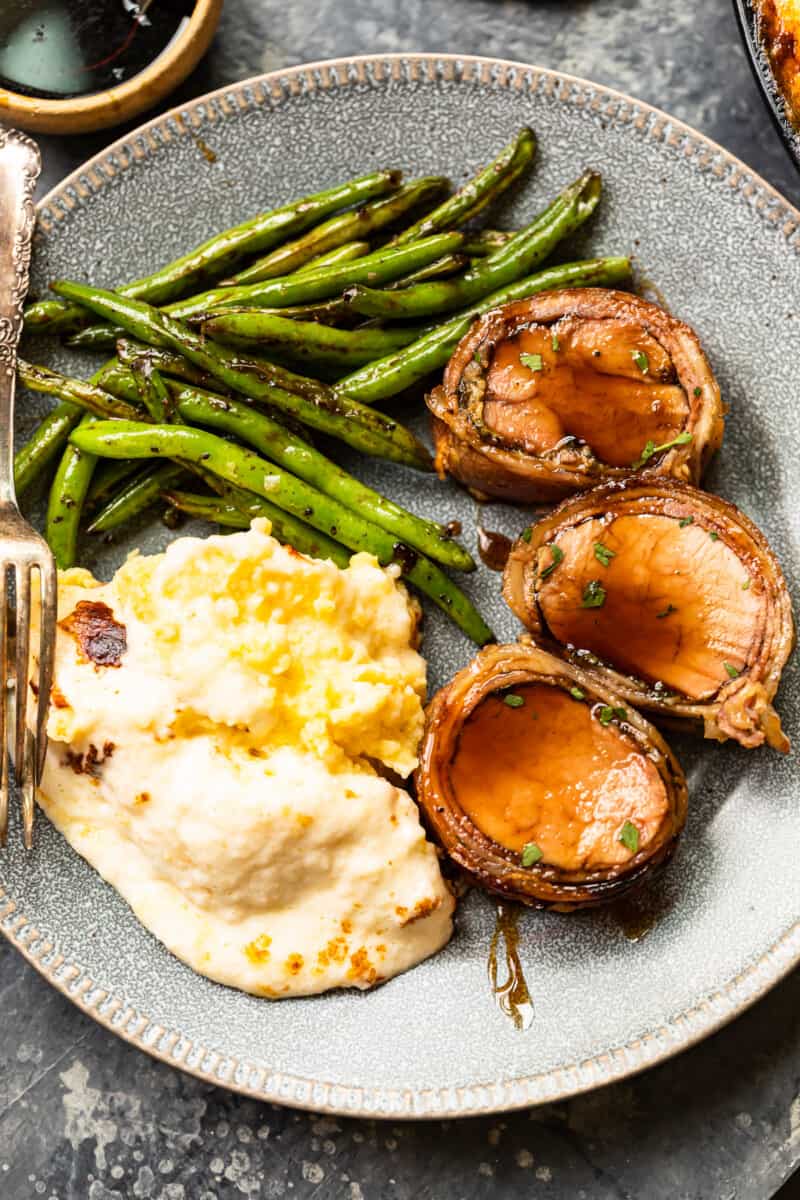slices of bacon wrapped pork tenderloin on a plate with mashed potatoes and vegetables