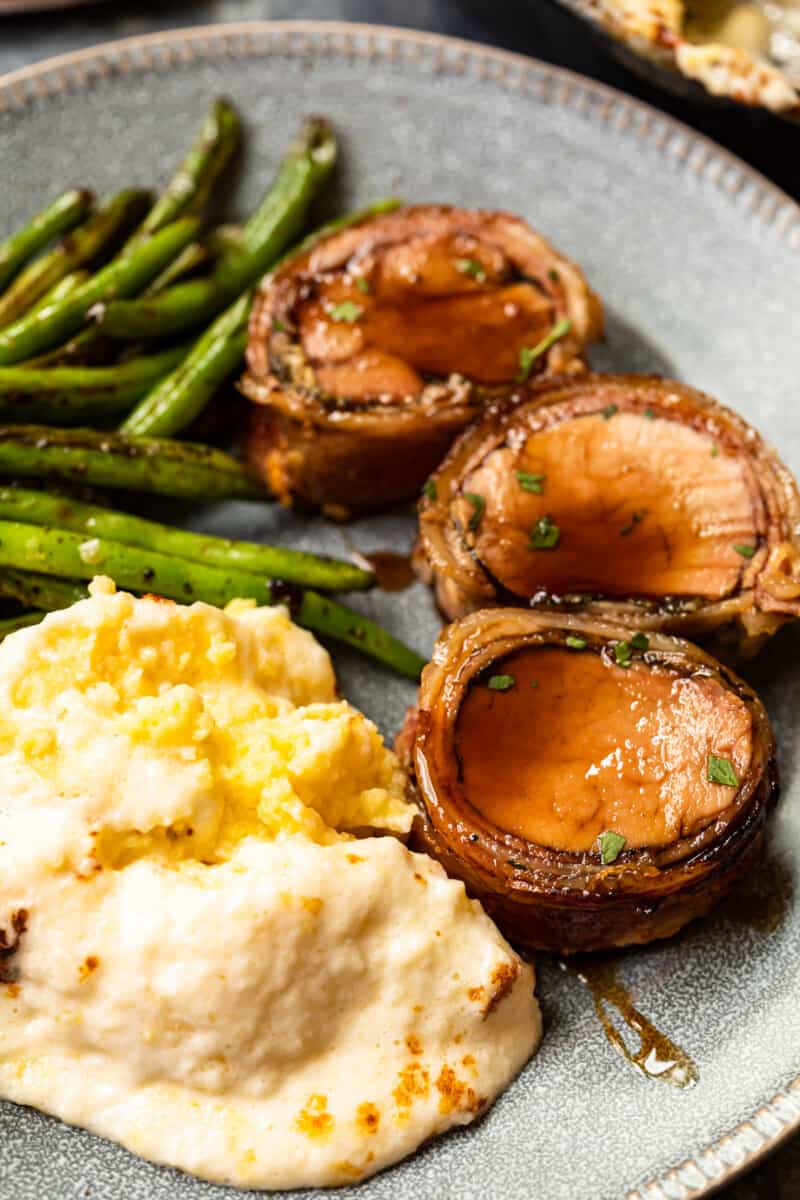 slices of bacon wrapped pork tenderloin on a plate with mashed potatoes and vegetables