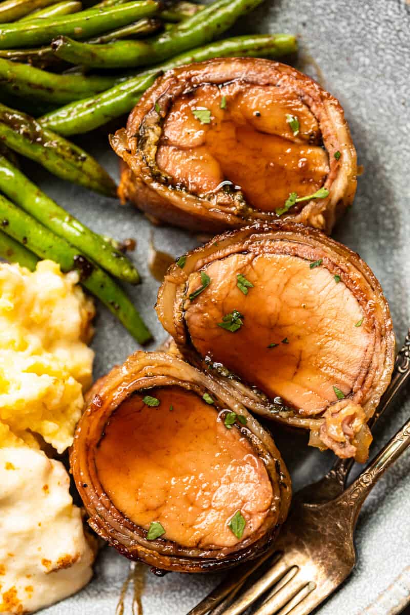 slices of bacon wrapped pork tenderloin on a plate with mashed potatoes and vegetables