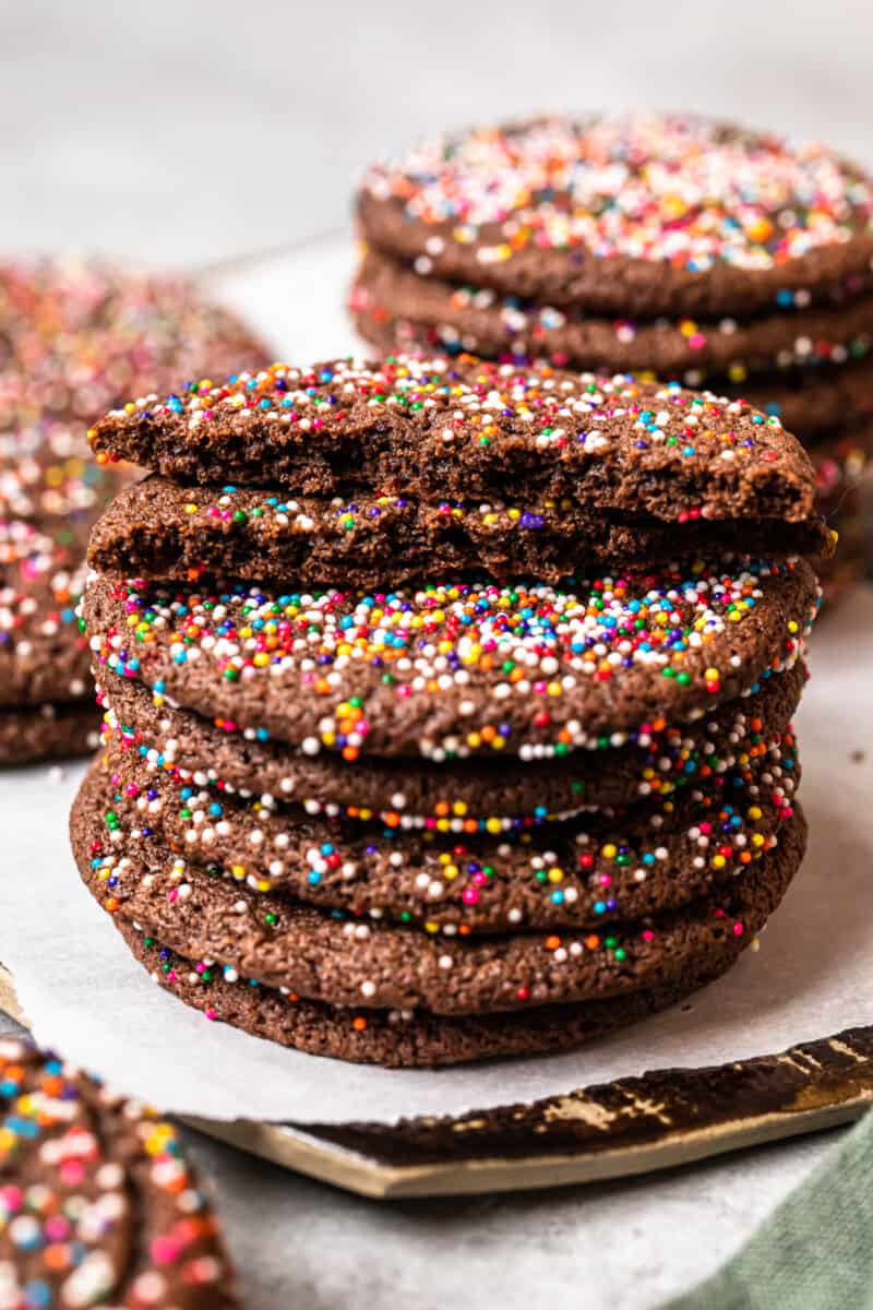 stack of 6 chocolate butter cookies on a white plate with the top cookie broken in half