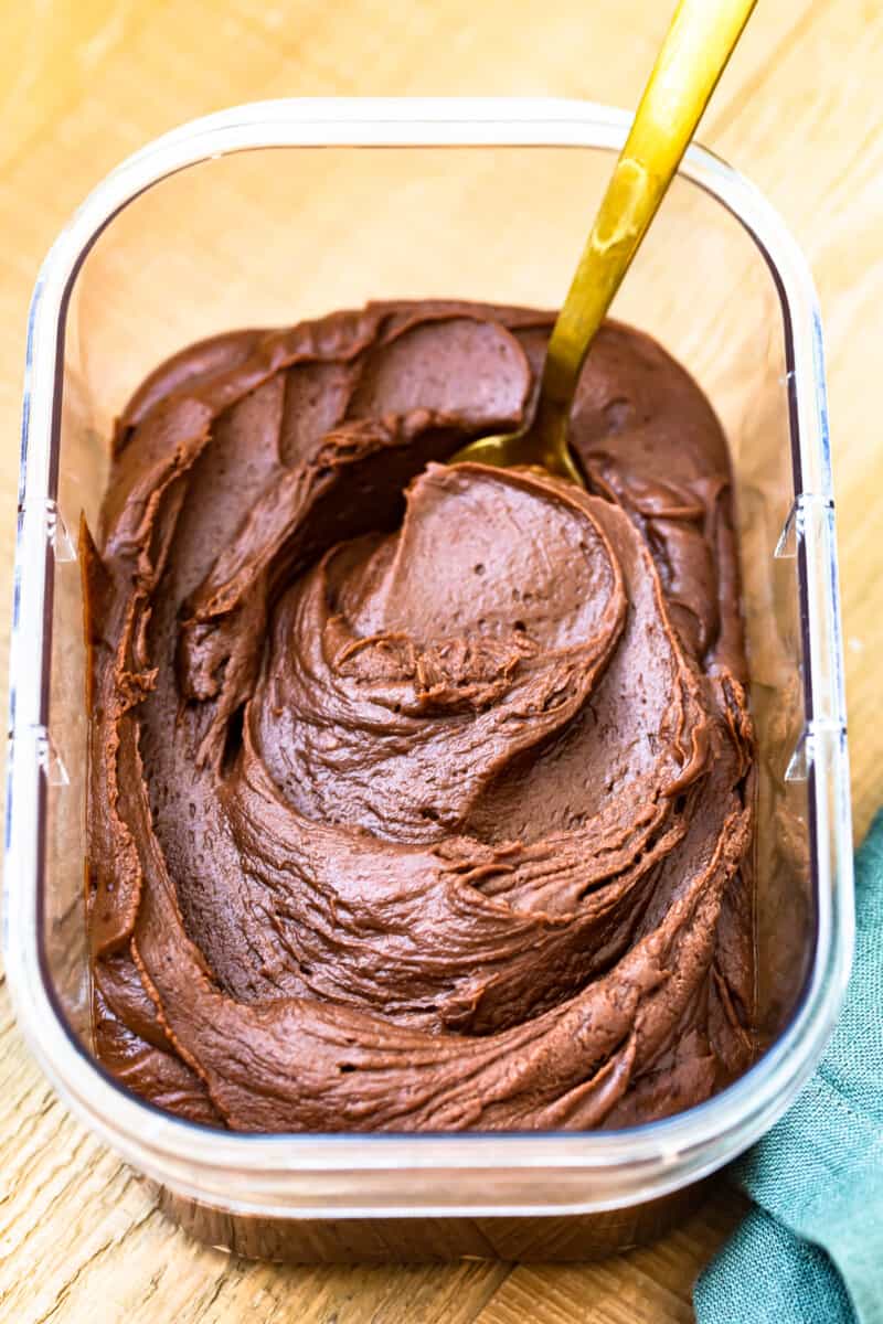 chocolate fudge frosting in a clear container with a serving spoon