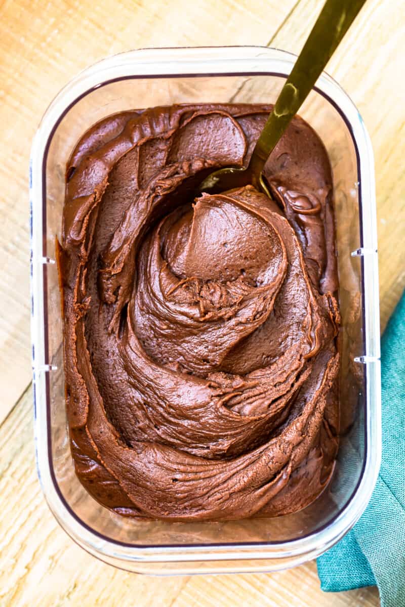 chocolate fudge frosting in a clear container with a serving spoon