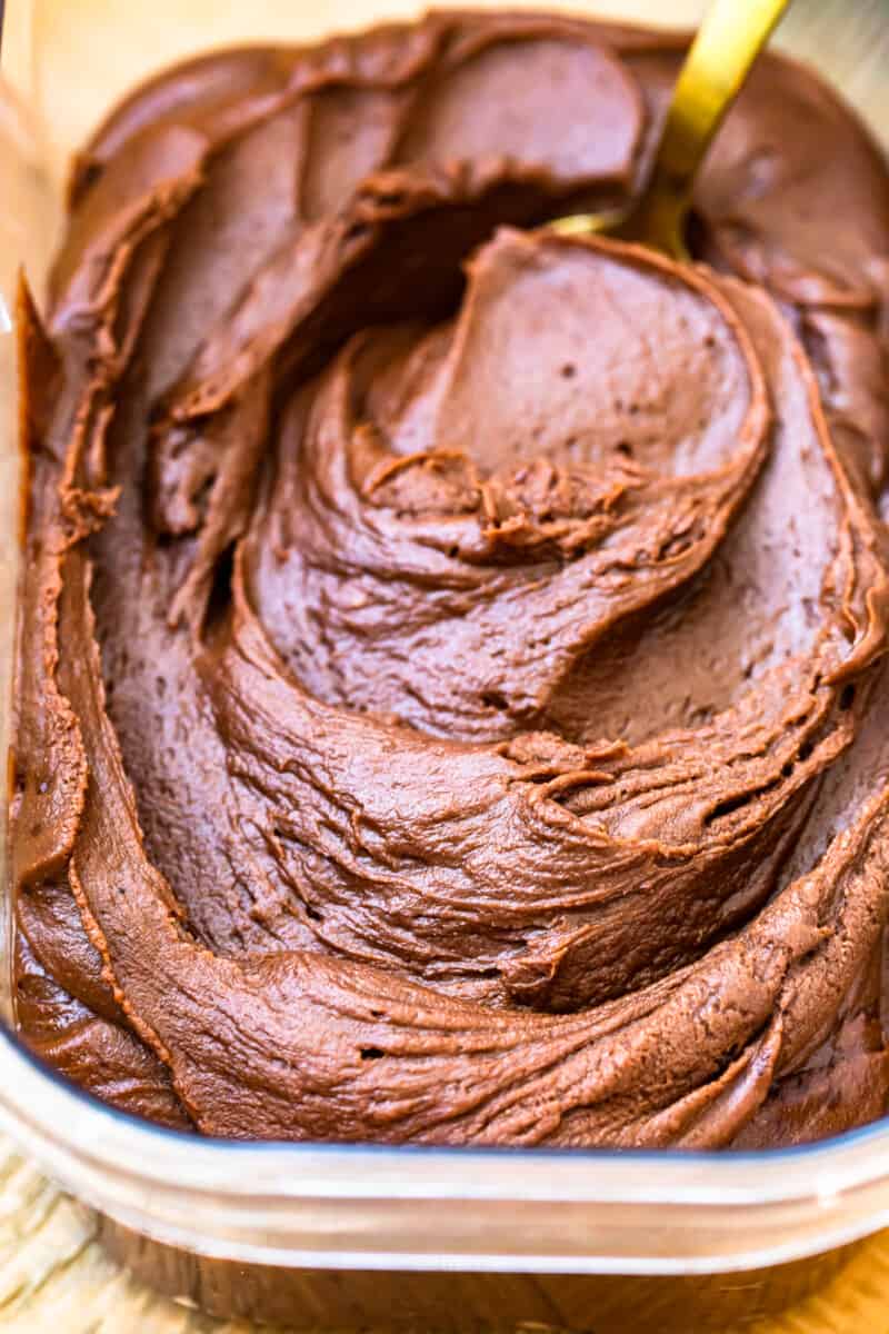 chocolate fudge frosting in a clear container with a serving spoon