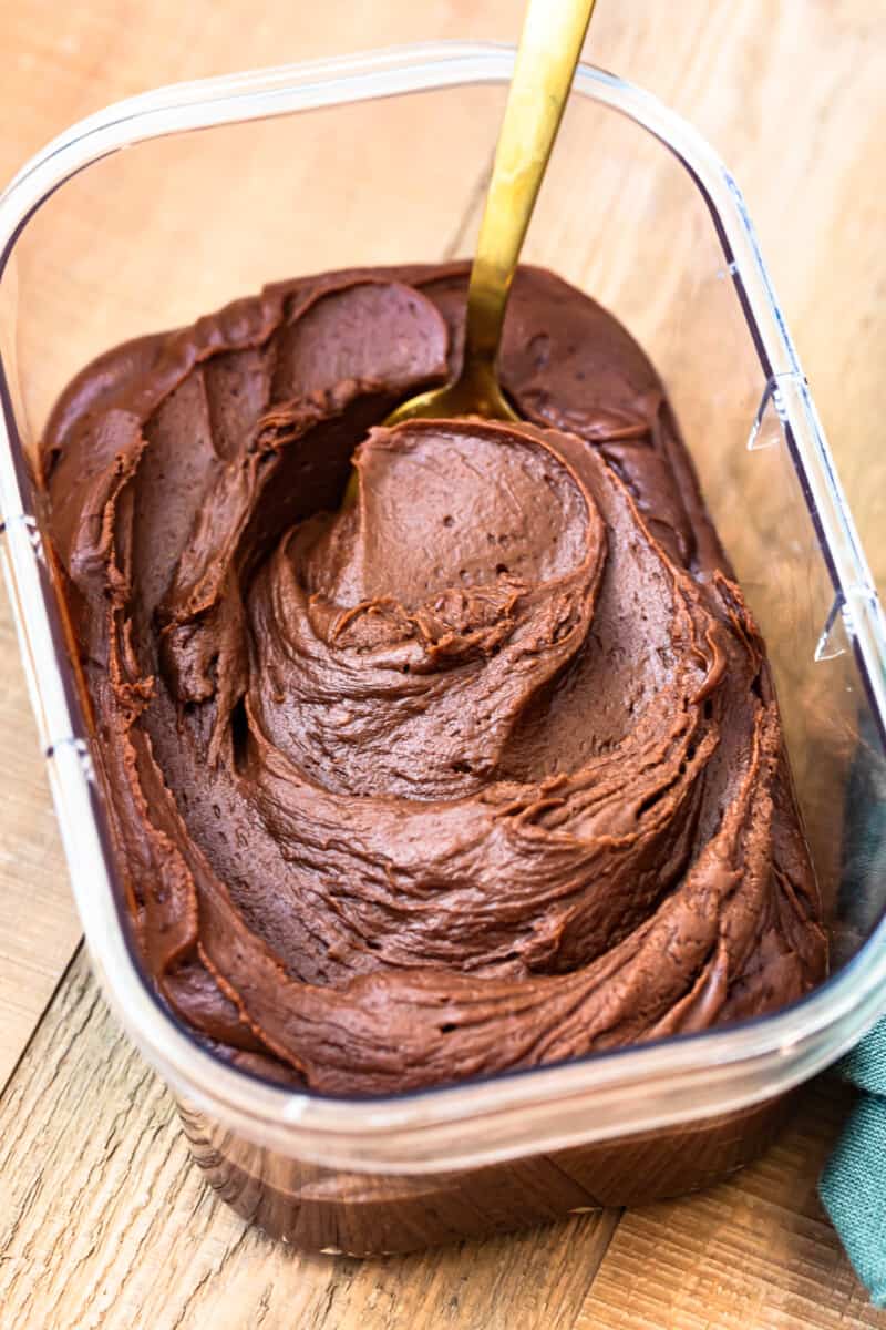 chocolate fudge frosting in a clear container with a serving spoon