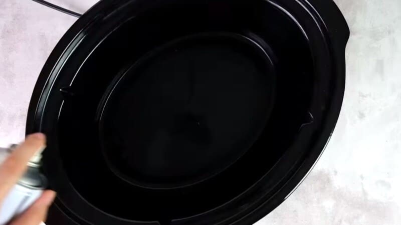 inside of a slow cooker being sprayed with non-stick spray