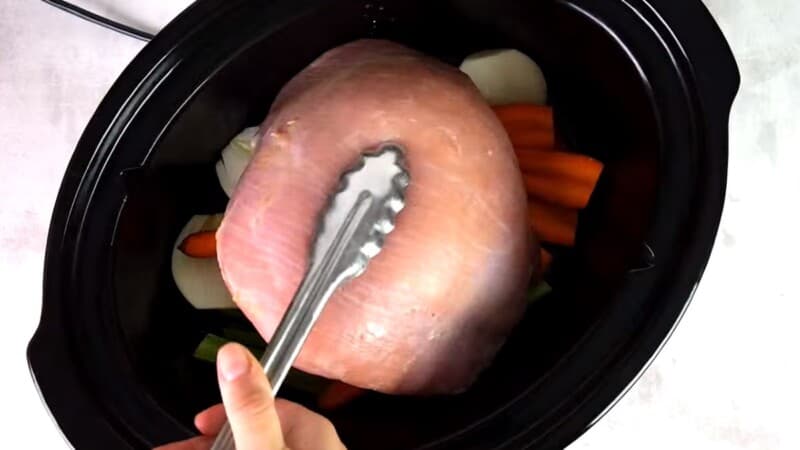 placing uncooked turkey breast inside of a slow cooker filled with vegetables