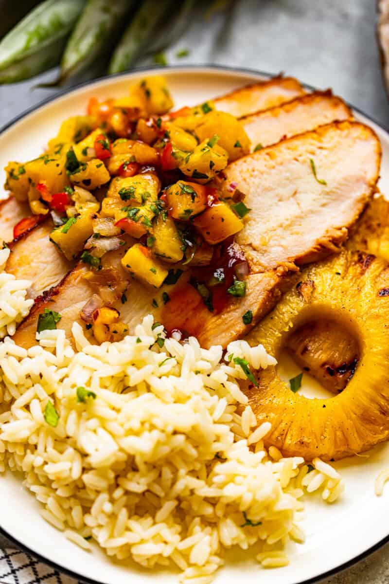 rice, grilled pineapple slices, and slices of huli huli turkey breast topped with pineapple salsa on a white plate