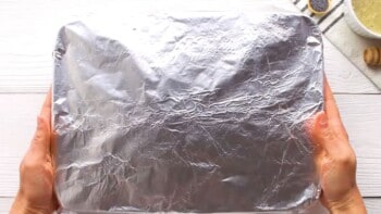 hands holding a baking dish wrapped in aluminum foil