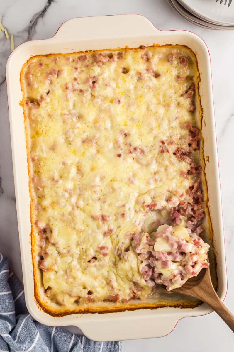 overhead image of ham and potato casserole with a wood spoon with a serving scooped out