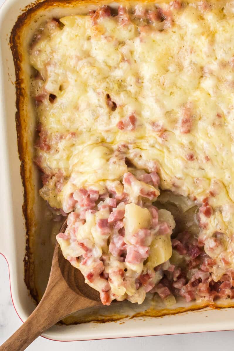 overhead image of ham and potato casserole with a wood spoon with a serving scooped out