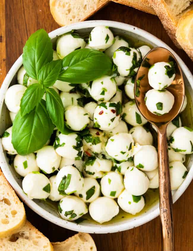 herb marinated mozzarella in white bowl with spoon
