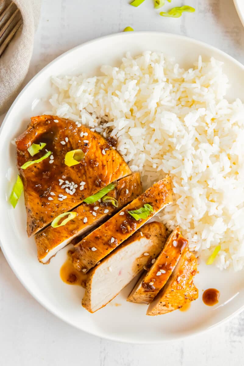 sliced honey garlic chicken breast on a white plate with rice