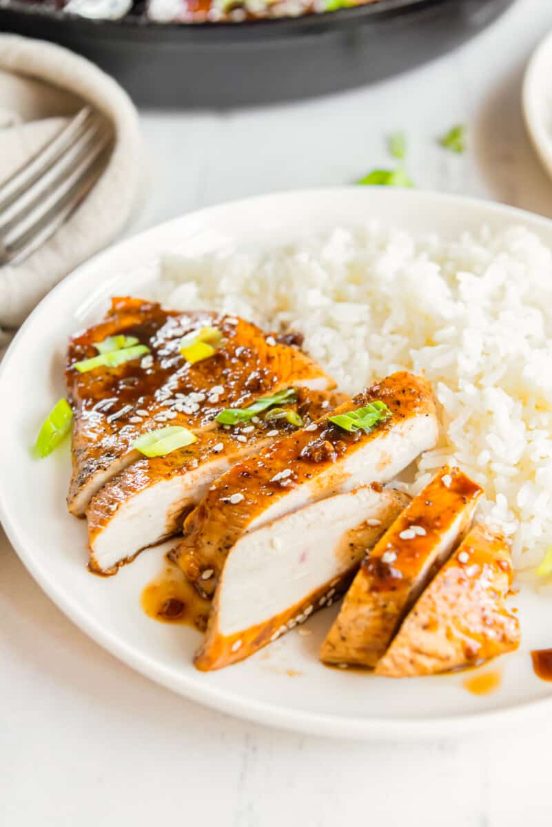 sliced honey garlic chicken breast on a white plate with rice