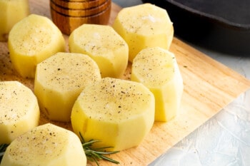 prepared fondant potatoes on a wood cutting board before cooking
