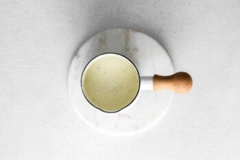 A cup of green sauce served on a white plate as part of a sheet pan Christmas dinner.