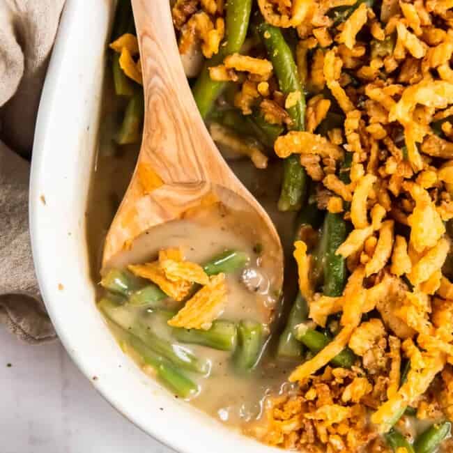 green bean casserole in a white casserole dish with a wood spoon