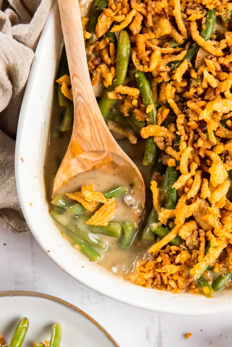 green bean casserole in a white casserole dish with a wood spoon