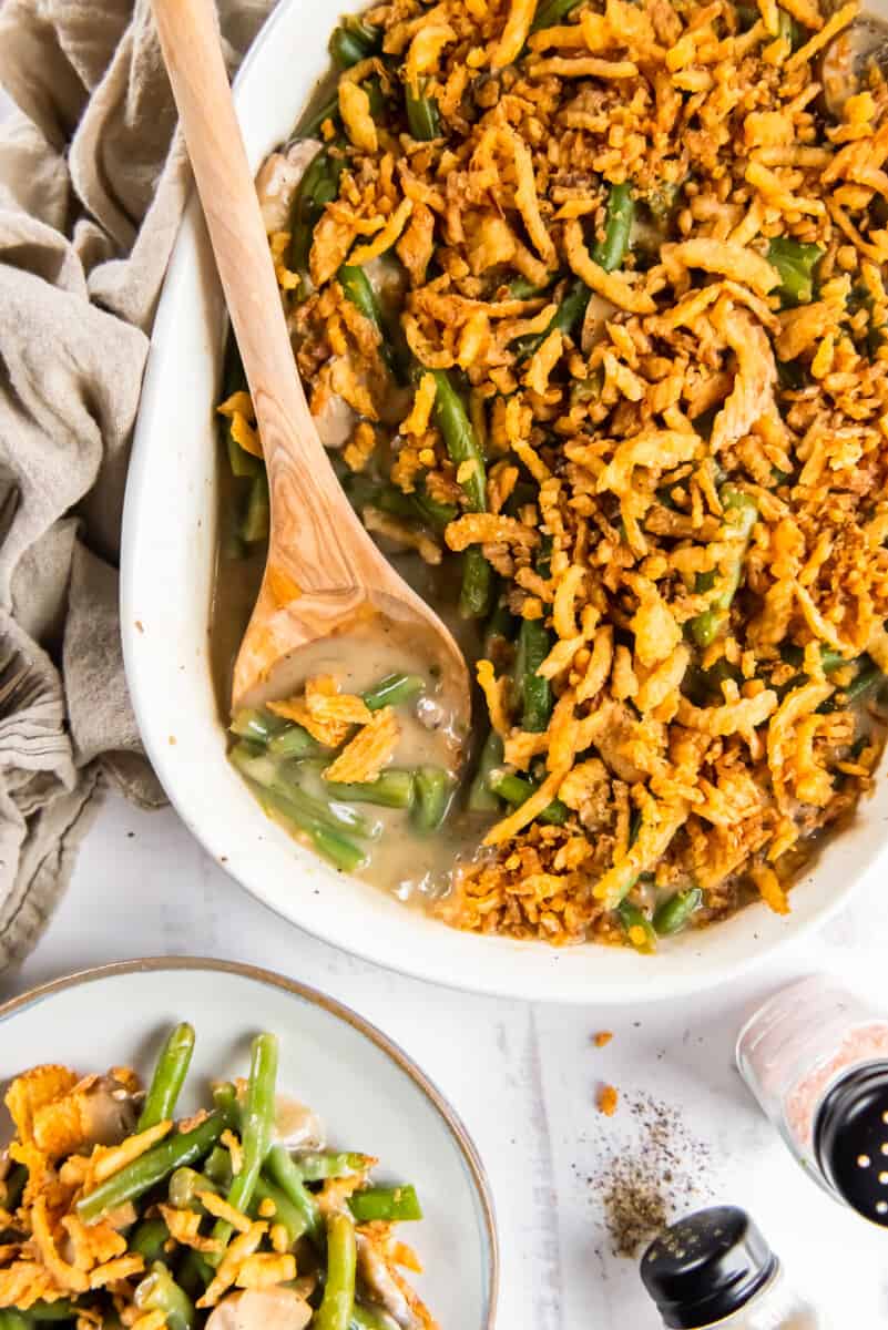 green bean casserole in a white casserole dish with a wood spoon