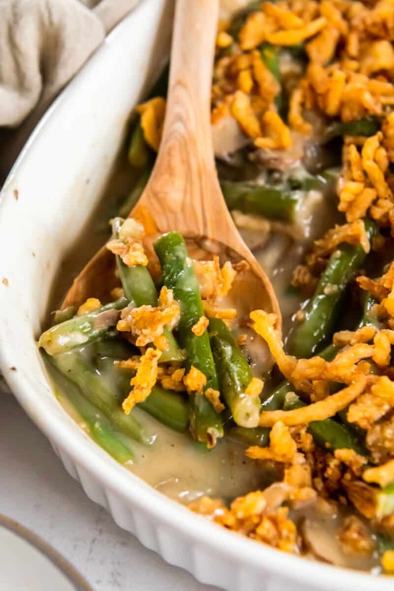 green bean casserole in a white casserole dish with a wood spoon