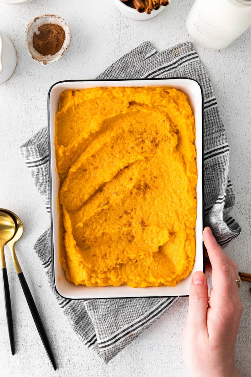hand holding a white baking dish filled with mashed sweet potatoes