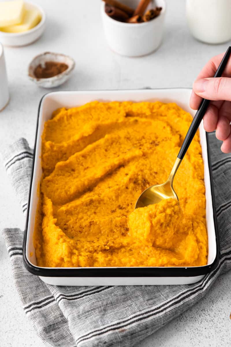 hand holding a spoon in a dish of mashed sweet potatoes