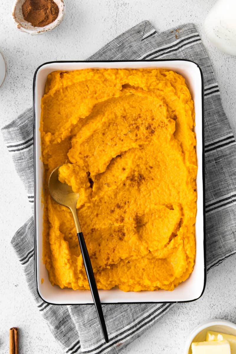 mashed sweet potatoes in a white rectangle baking dish with a serving spoon