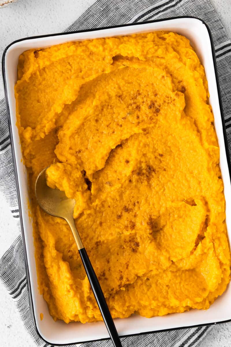 mashed sweet potatoes in a white rectangle baking dish with a serving spoon