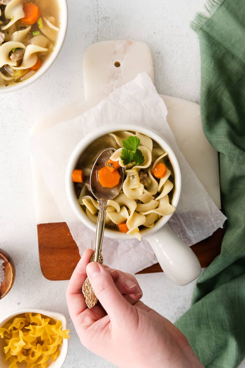 turkey noodle soup in a white bowl with a hand holding a spoon