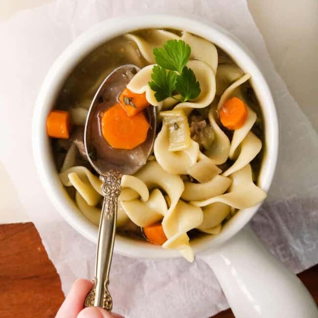 turkey noodle soup in a white bowl with a hand holding a spoon
