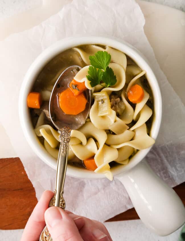 turkey noodle soup in a white bowl with a hand holding a spoon