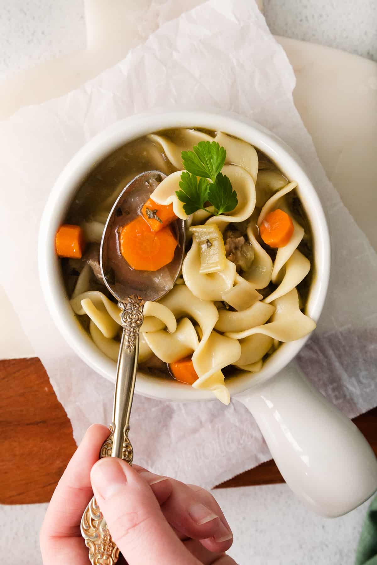 turkey noodle soup in a white bowl with a hand holding a spoon