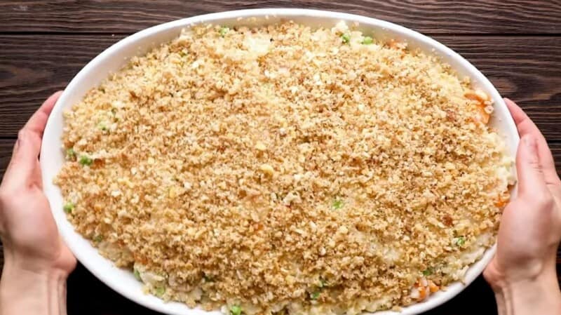 two hands holding a large casserole dish filled with turkey casserole