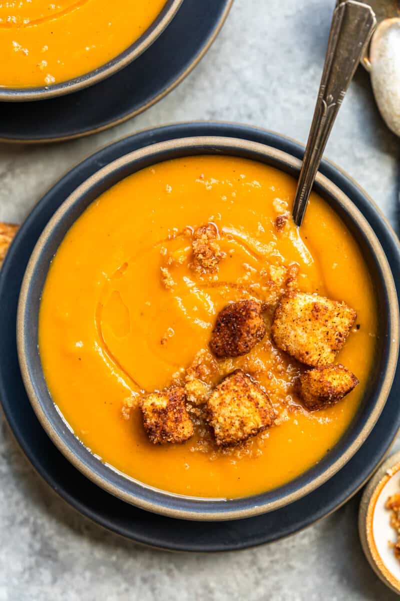 roasted butternut squash soup topped with cinnamon croutons in a black bowl with a spoon