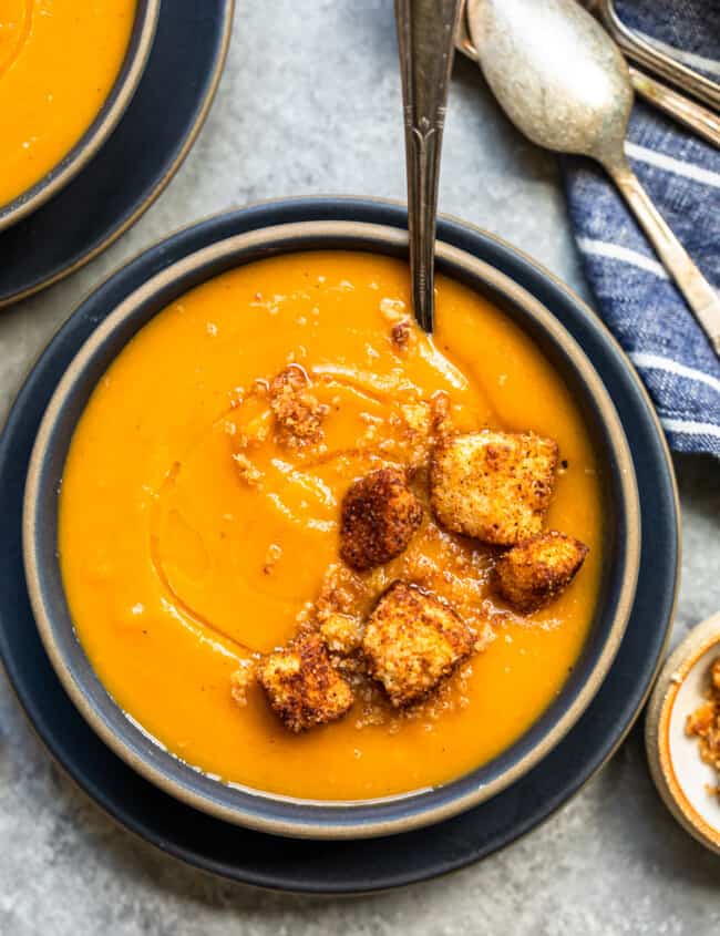 roasted butternut squash soup topped with cinnamon croutons in a black bowl with a spoon