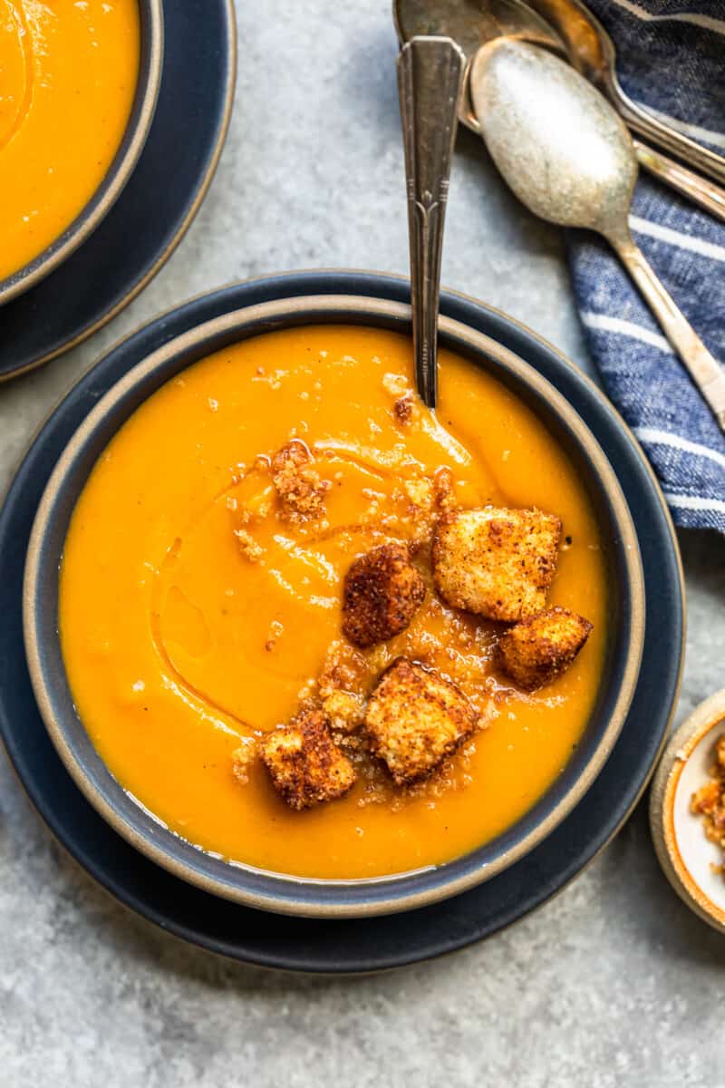 roasted butternut squash soup topped with cinnamon croutons in a black bowl with a spoon