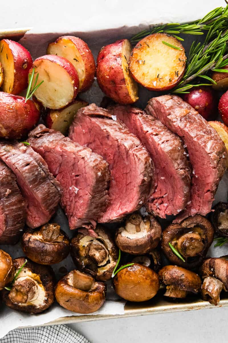 sheet pan with slices of beef tenderloin and roasted red potatoes and mushrooms