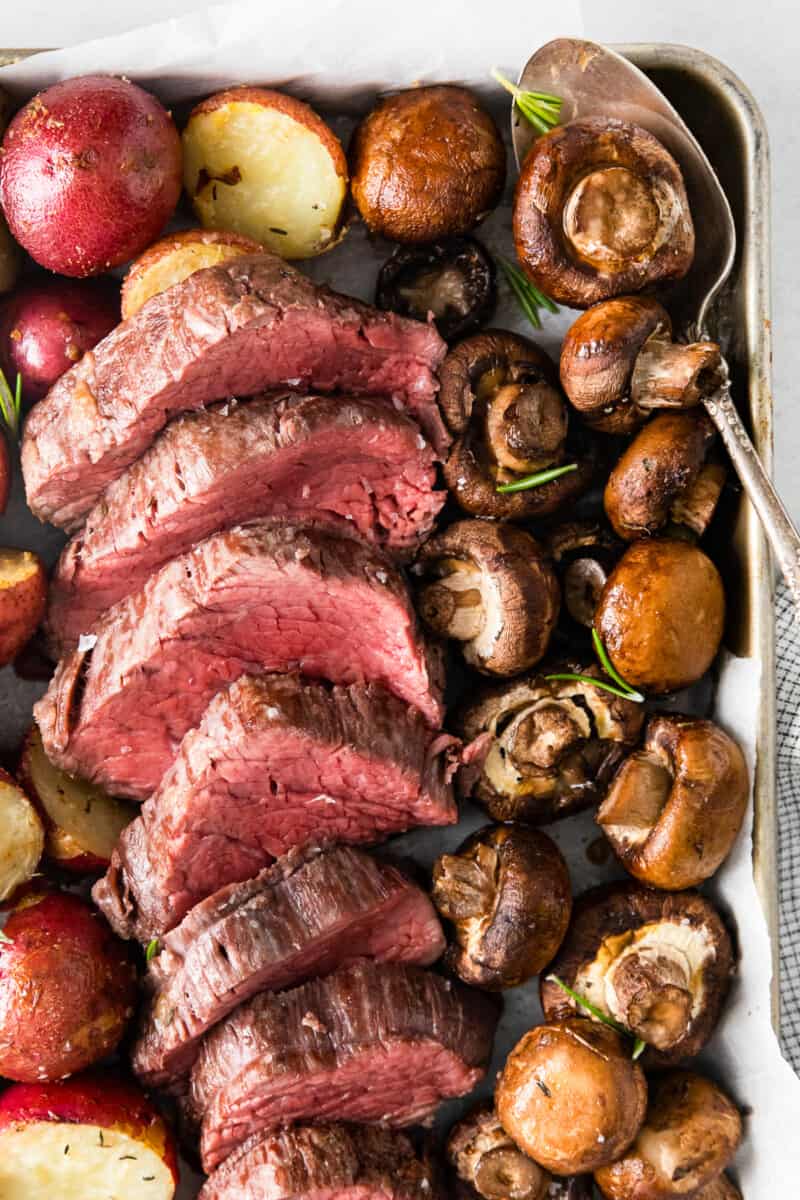sliced beef tenderloin and roasted mushrooms and red potatoes on a sheet pan