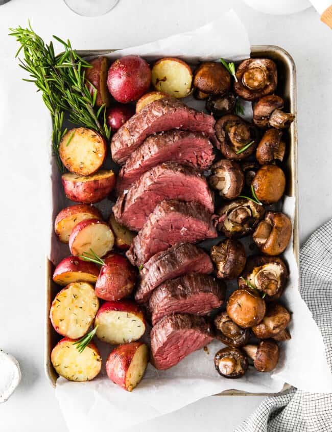 sheet pan with slices of beef tenderloin and roasted red potatoes and mushrooms