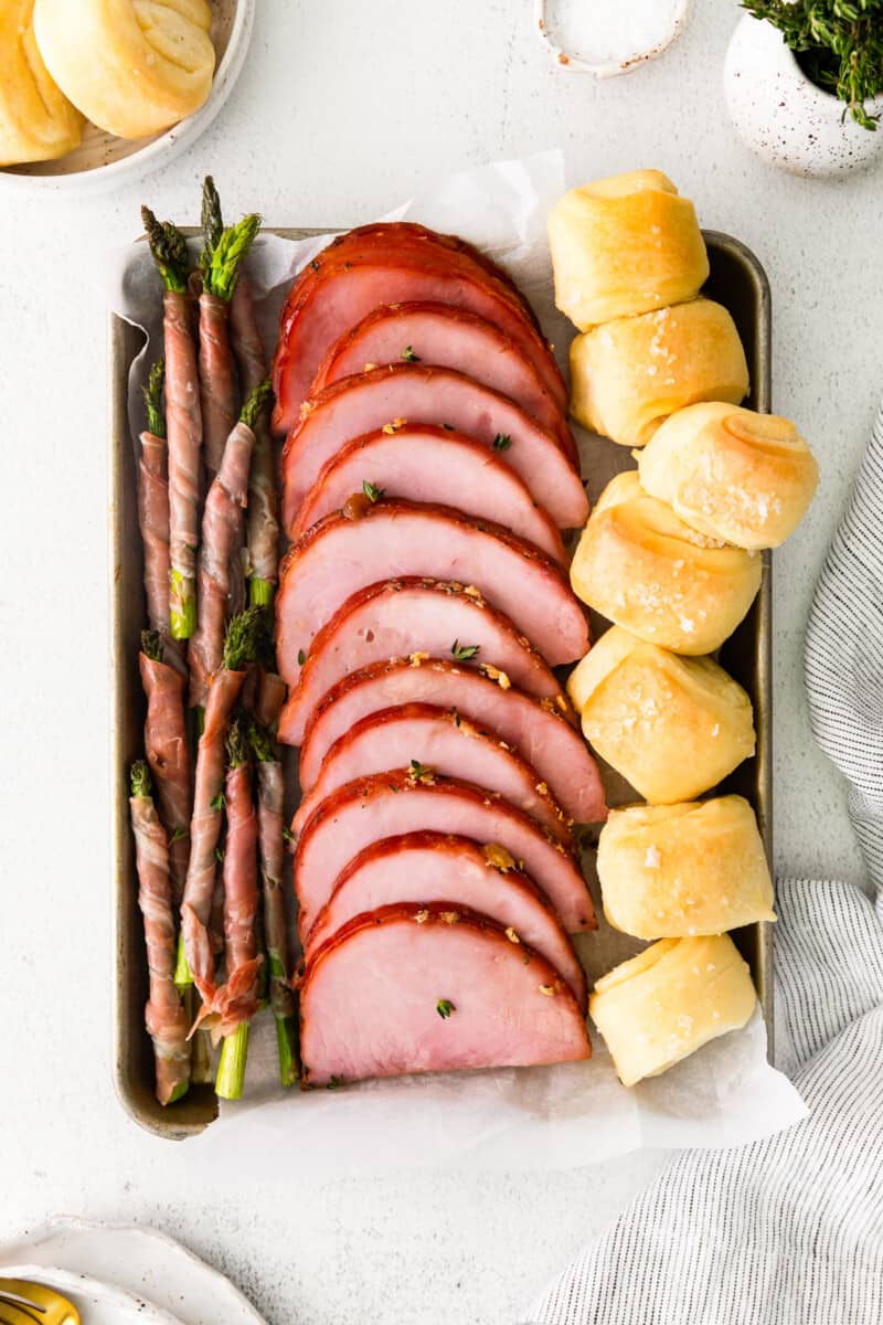 ham, prosciutto wrapped asparagus, and rolls on a sheet pan after baking