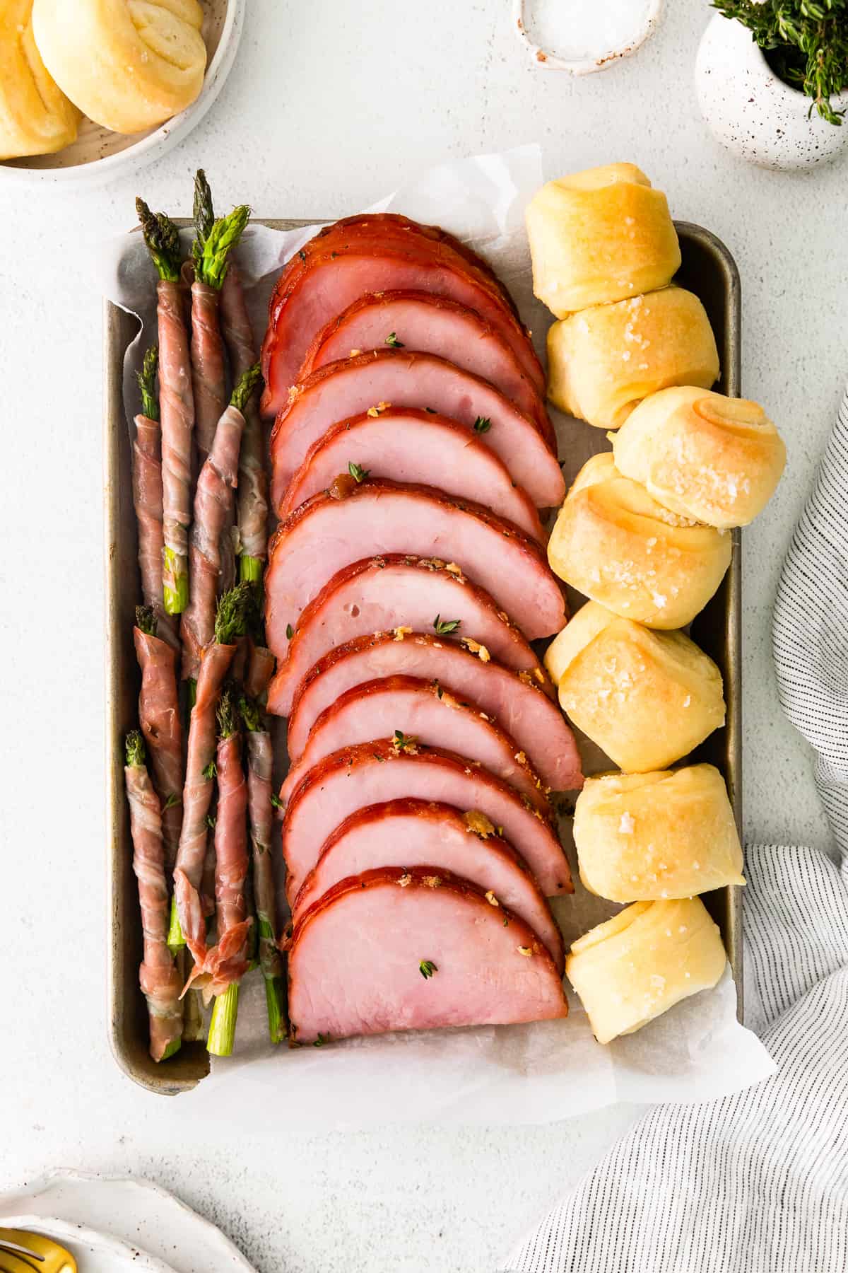 ham, prosciutto wrapped asparagus, and rolls on a sheet pan after baking.