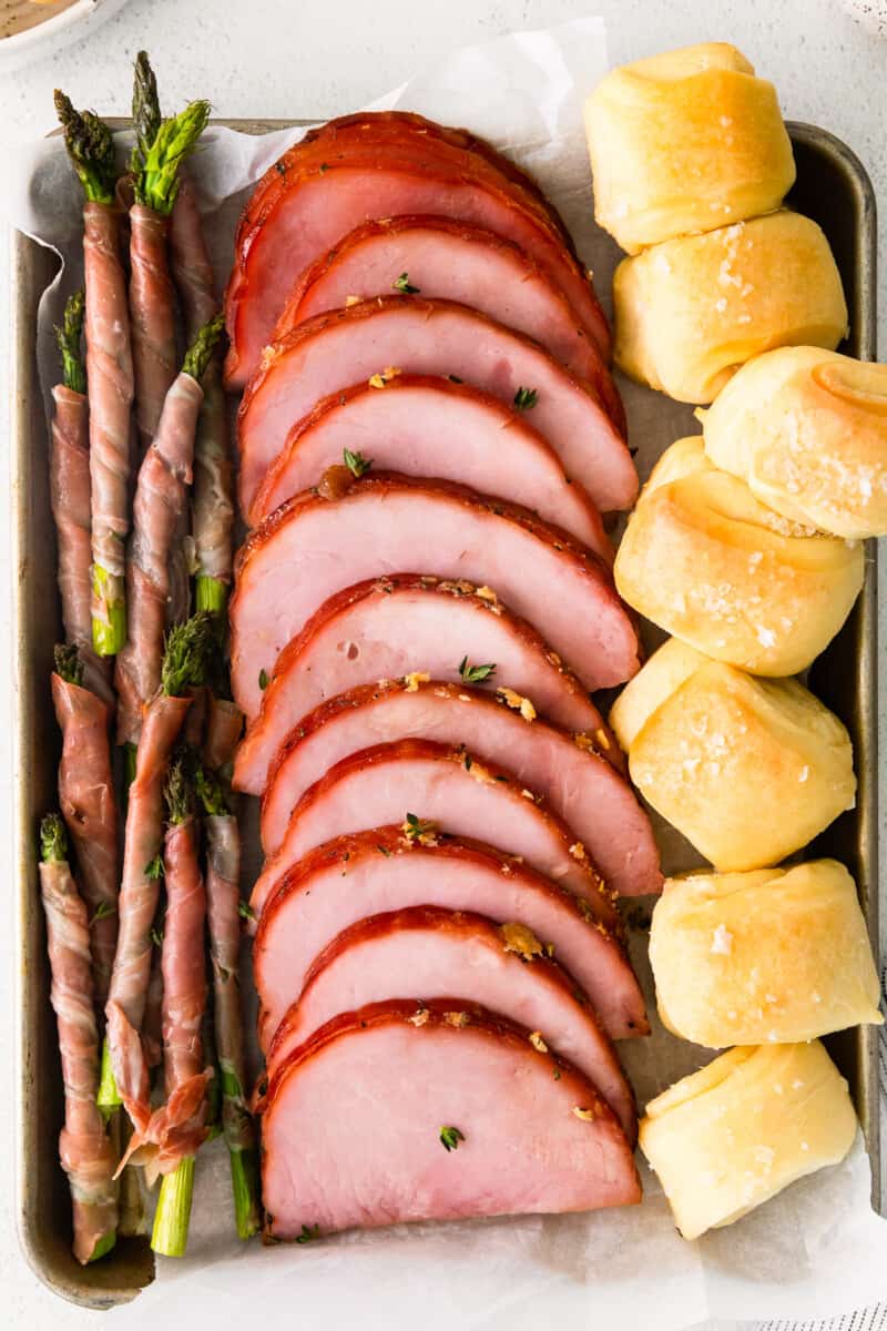 ham, prosciutto wrapped asparagus, and rolls on a sheet pan after baking
